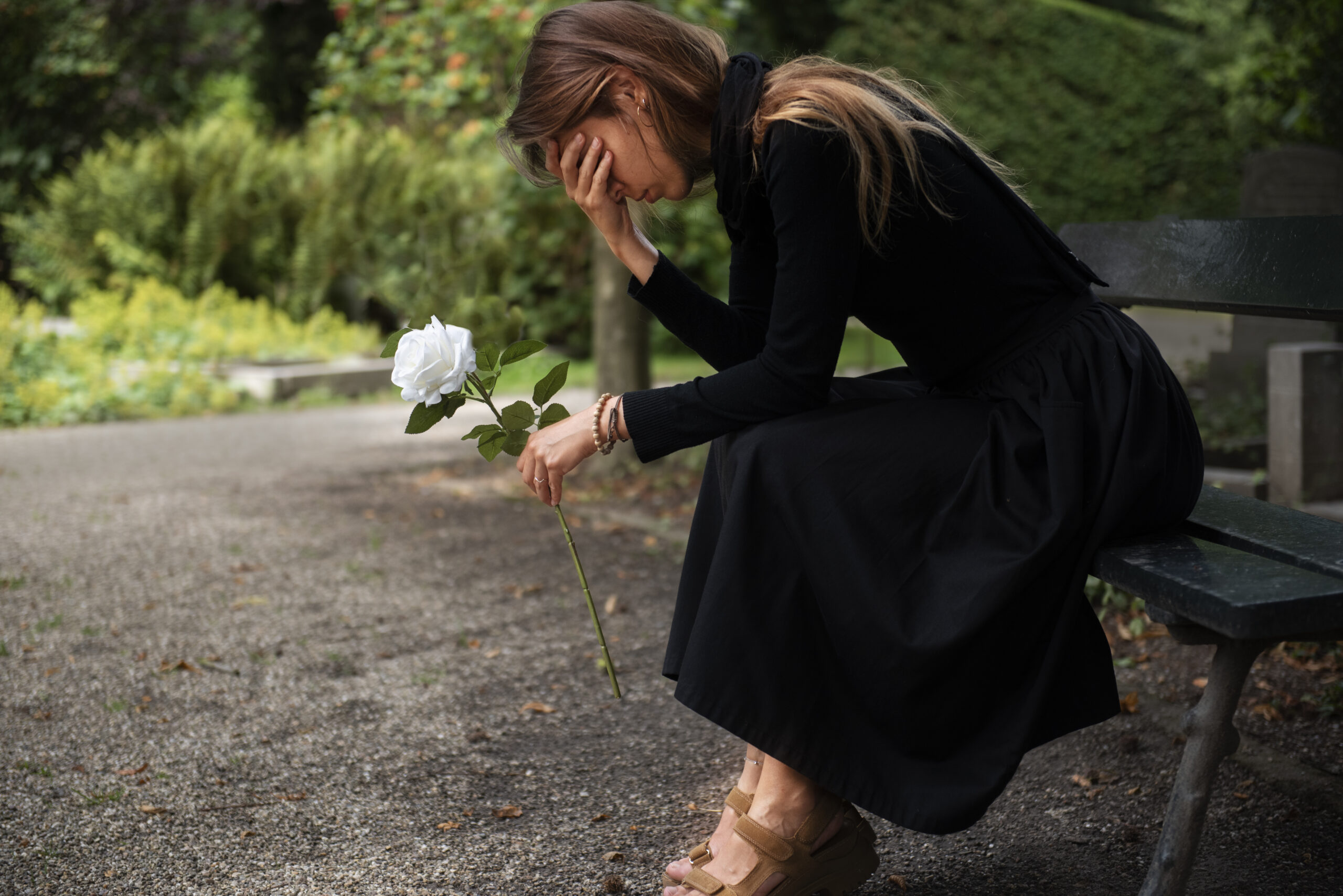 Grieving woman holding a white rose on a bench, symbolizing loss and healing through grief counseling in Houston, TX.