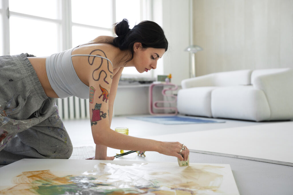 Woman painting on the floor in a bright studio, illustrating creative practice and letting go of perfectionism for Christian women in Frisco Texas