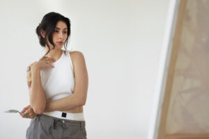 “Woman thoughtfully standing in front of a canvas while painting, representing reflection and creativity in overcoming perfectionism.”