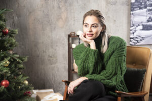 Woman sitting thoughtfully beside a Christmas tree, reflecting during the holidays
