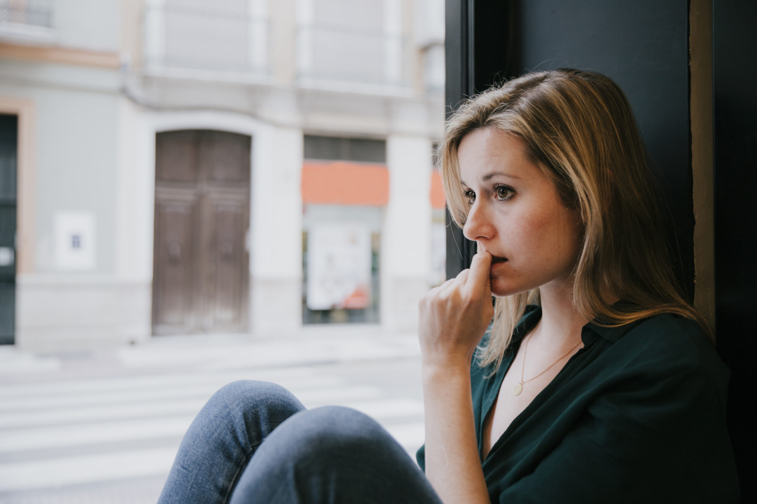 Woman sitting by a window feeling emotional burnout and reflecting on faith-based self-care.