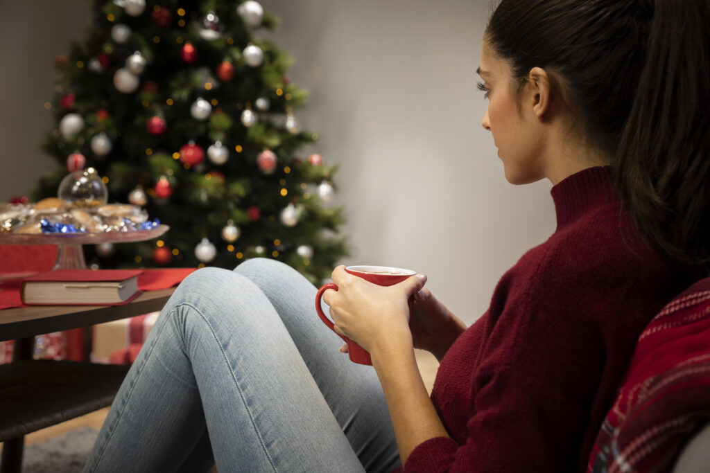 Woman sitting quietly with a mug near a Christmas tree, reflecting during the holiday season and symbolizing depression during the Christmas season