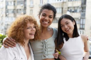 Three friends smiling together outdoors, representing community support and healing.