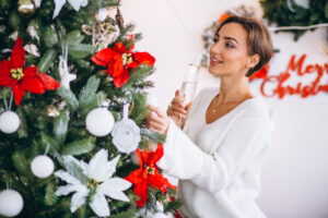 Woman decorating a Christmas tree while holding a drink, representing moments of self-care and emotional support during the holiday season