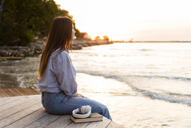 Side view of a woman looking at the sunset over the ocean, symbolizing calm, reflection, and emotional wellness during therapy for anxiety and panic attacks