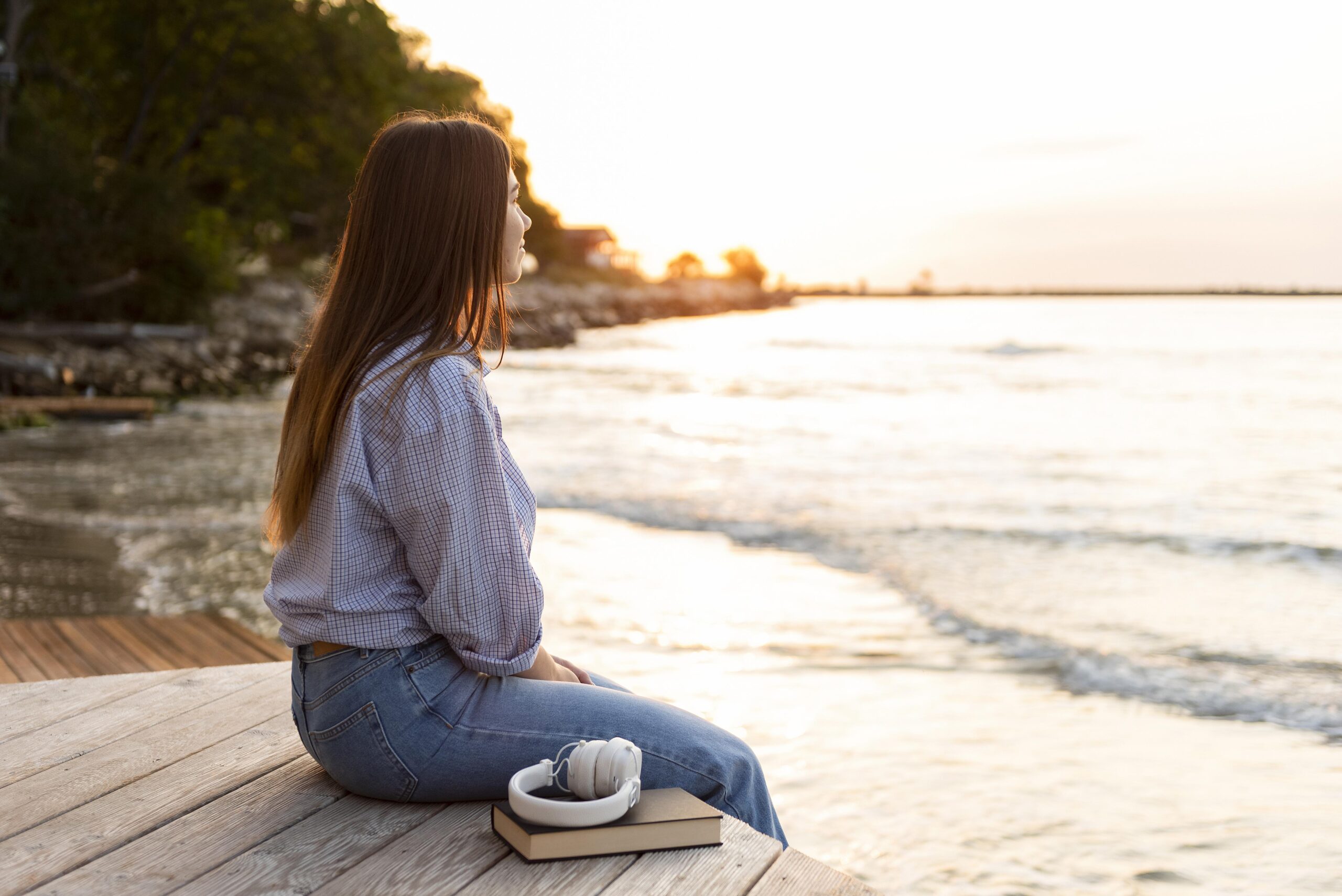 Side view of a woman looking at the sunset over the ocean, symbolizing calm, reflection, and emotional wellness during therapy for anxiety and panic attacks