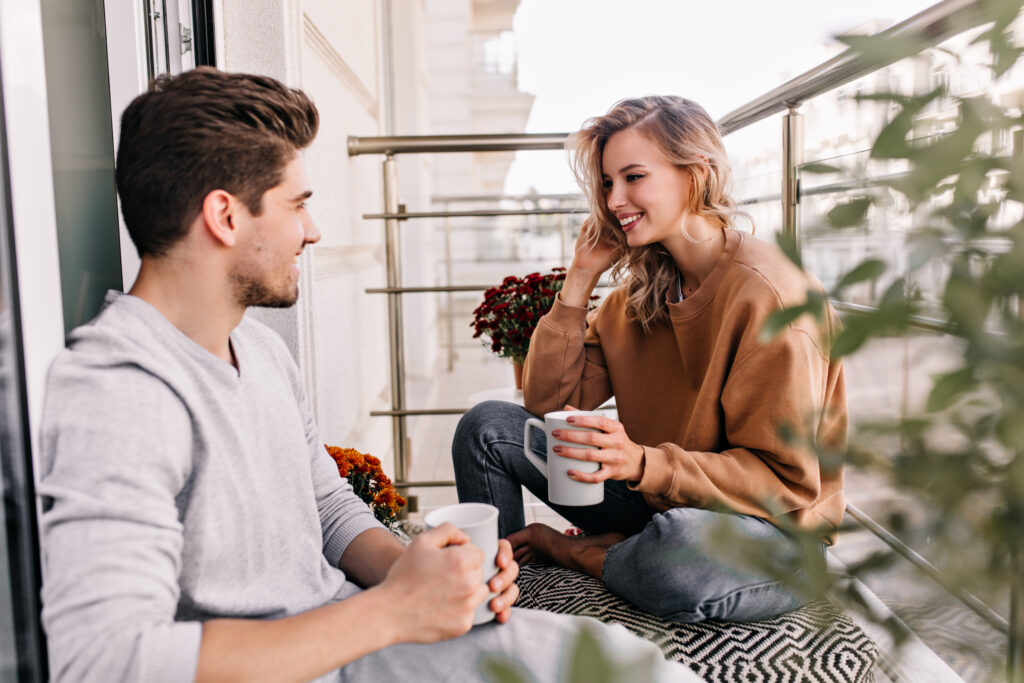 Husband and wife sitting together on a balcony having a warm conversation over coffee, representing healthy marriage communication