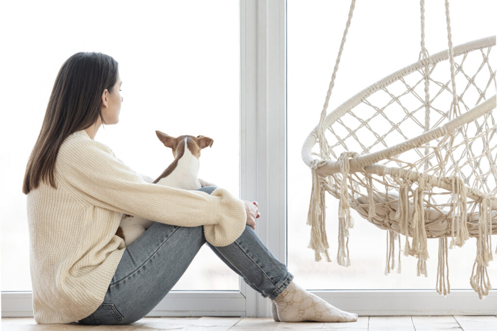 Woman sitting quietly by a window, reflecting, representing the grief of growing up with an absent or unavailable parent.