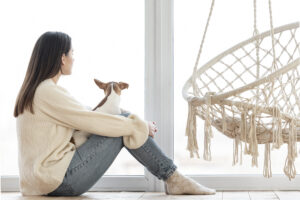 Woman sitting quietly by a window, reflecting, representing the grief of growing up with an absent or unavailable parent.