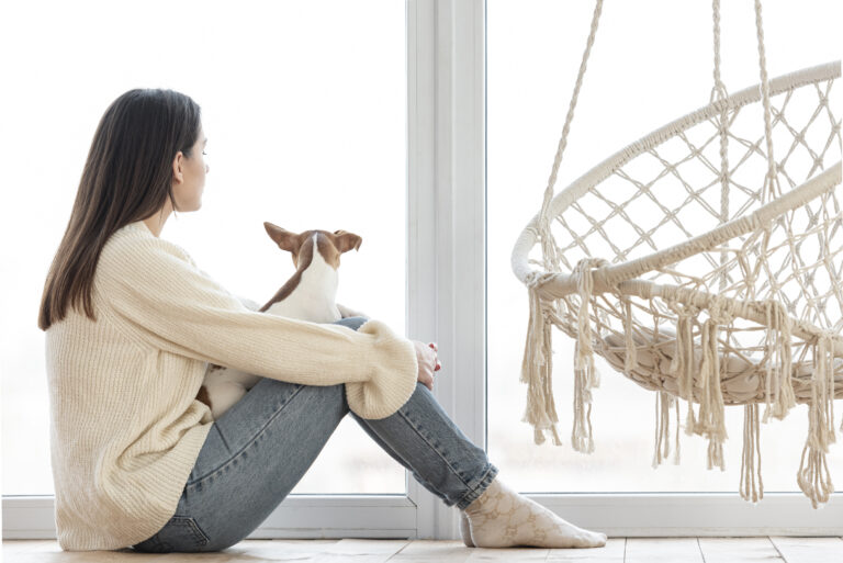Woman sitting quietly by a window, reflecting, representing the grief of growing up with an absent or unavailable parent.